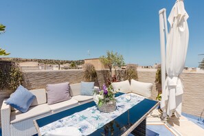 A rooftop terrace with a pool, white outdoor furniture, and a white umbrella.