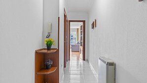 A hallway with a radiator, wooden shelves with plants, and a door leading to a room.