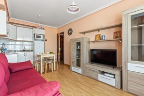 Un soggiorno con divano rosso, televisione, angolo cottura e tavolo da pranzo.