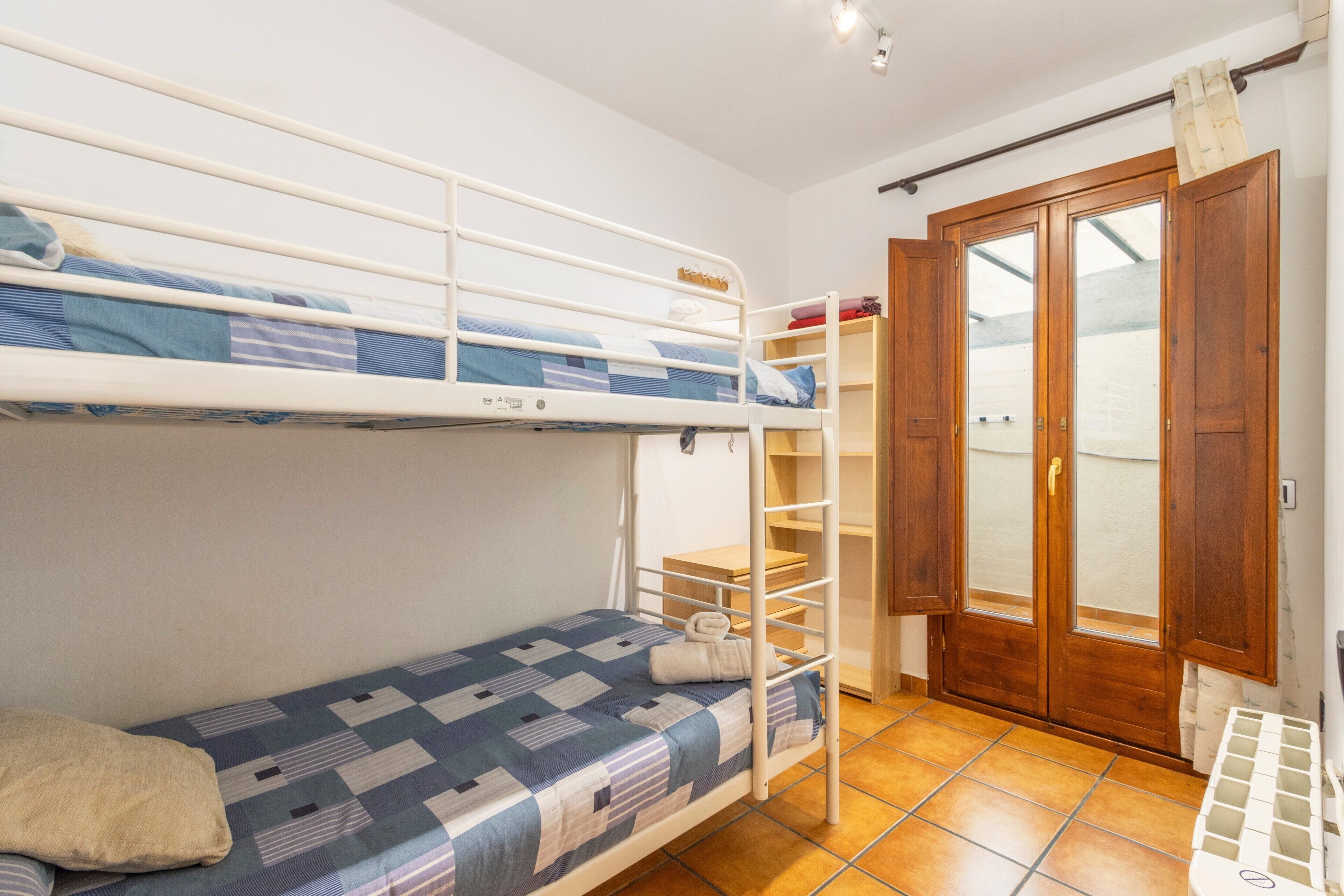 A bunk bed room with a wooden door, a small shelf, and a tiled floor.