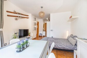 A compact living space with a dining table, sofa, TV, and skis on the wall. - Apartment 'Potxó' with Mountain Views, Balcony and Wi-Fi (La Bastida de Sort)