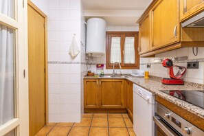 A kitchen with wooden cabinets, a built-in oven, a dishwasher, and a red kettle on the countertop. - Apartment 'Potxó' with Mountain Views, Balcony and Wi-Fi (La Bastida de Sort)