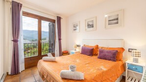 Ein Schlafzimmer mit Bett, Nachttisch, Lampe und einem Fenster mit Vorhängen.
