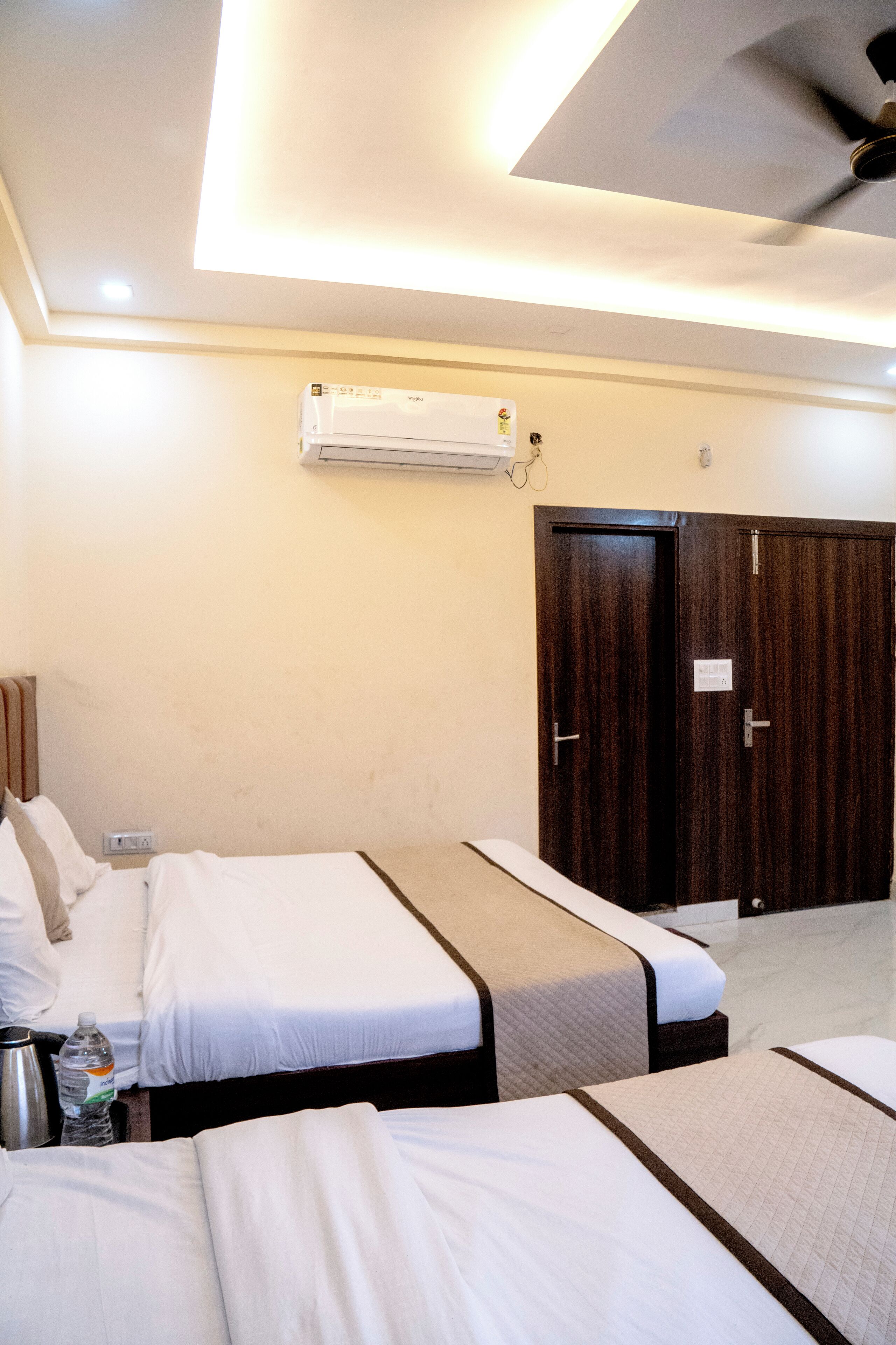 Ein Hotelzimmer mit zwei Betten, einem Deckenventilator, einer Klimaanlage und einem dunklen Holzschrank.