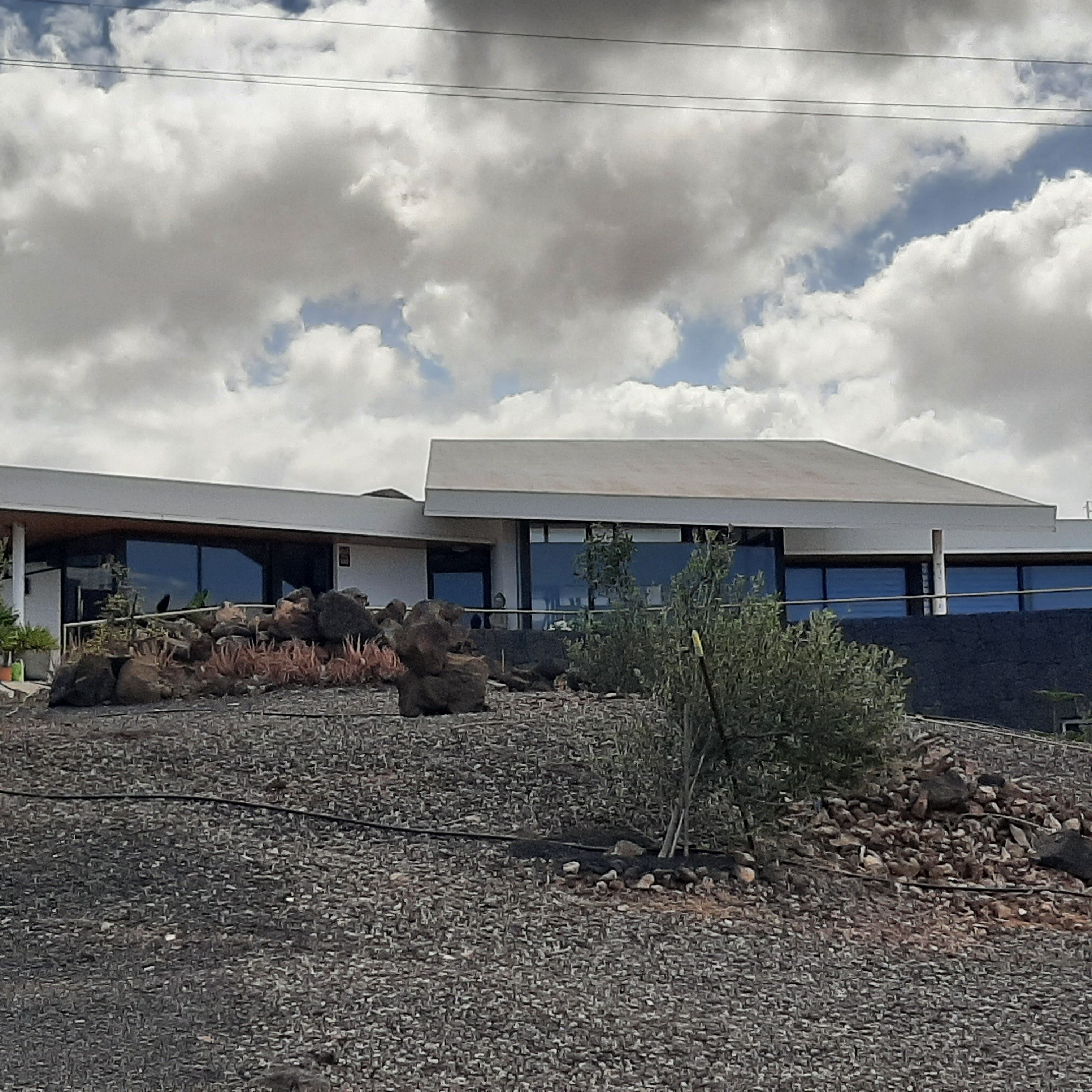 Un bâtiment moderne doté d’un toit plat et de grandes fenêtres, entouré d’un paysage rocheux et d’une végétation clairsemée.