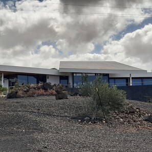 A modern building with a flat roof and large windows, surrounded by a rocky landscape and sparse vegetation. - Apartment Atlantis with Sea View, Wi-Fi and Air Conditioning (Las Breñas)