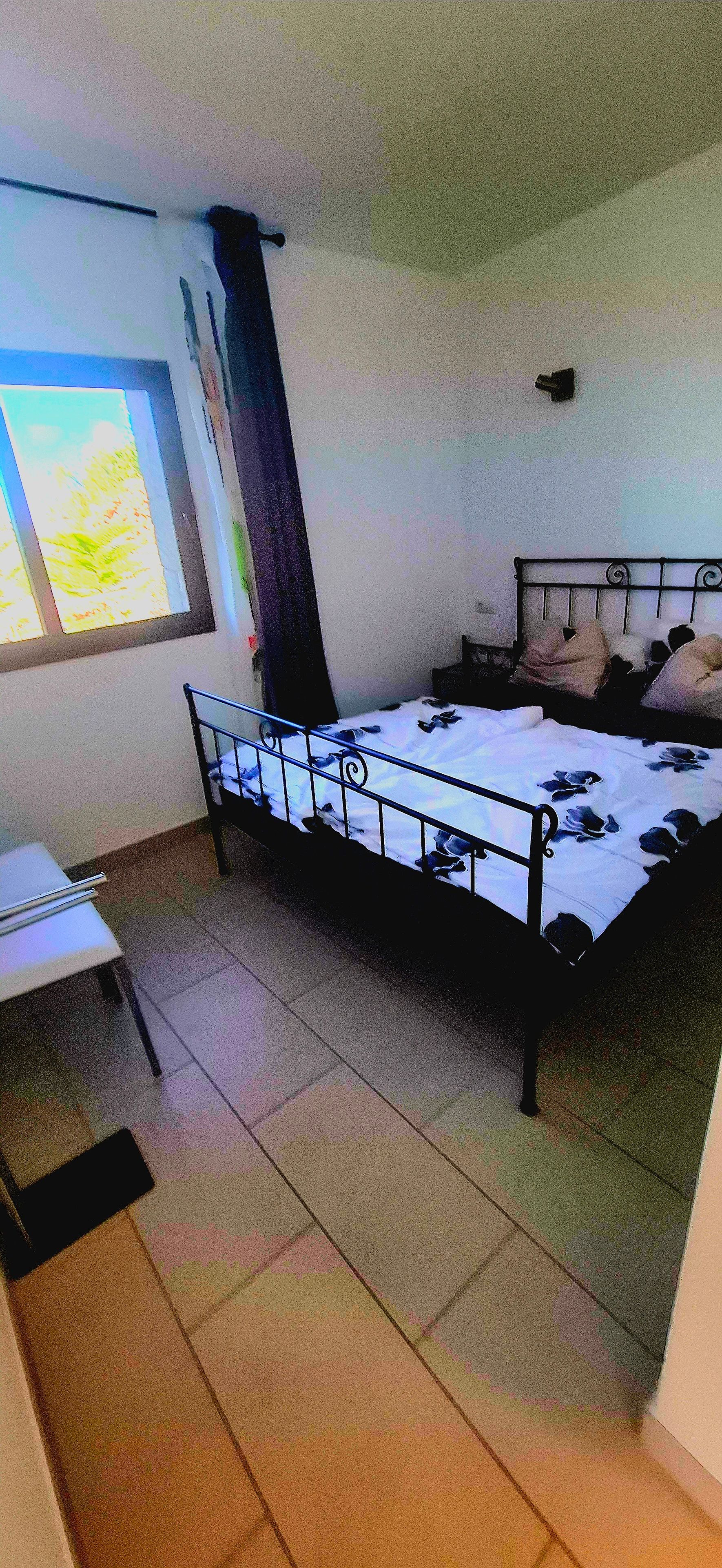 Une chambre à coucher avec un lit, une fenêtre, une chaise et une petite table.
