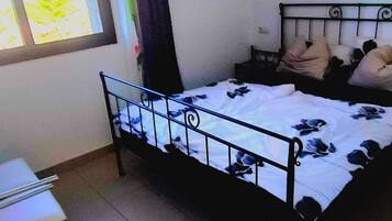 Un dormitorio con cama, ventana, silla y una mesita.