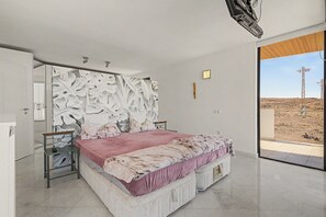 A modern bedroom with a large bed, a nightstand, a mirror, and a view of the desert through a glass door. - Apartment Atlantis with Sea View, Wi-Fi and Air Conditioning (Las Breñas)