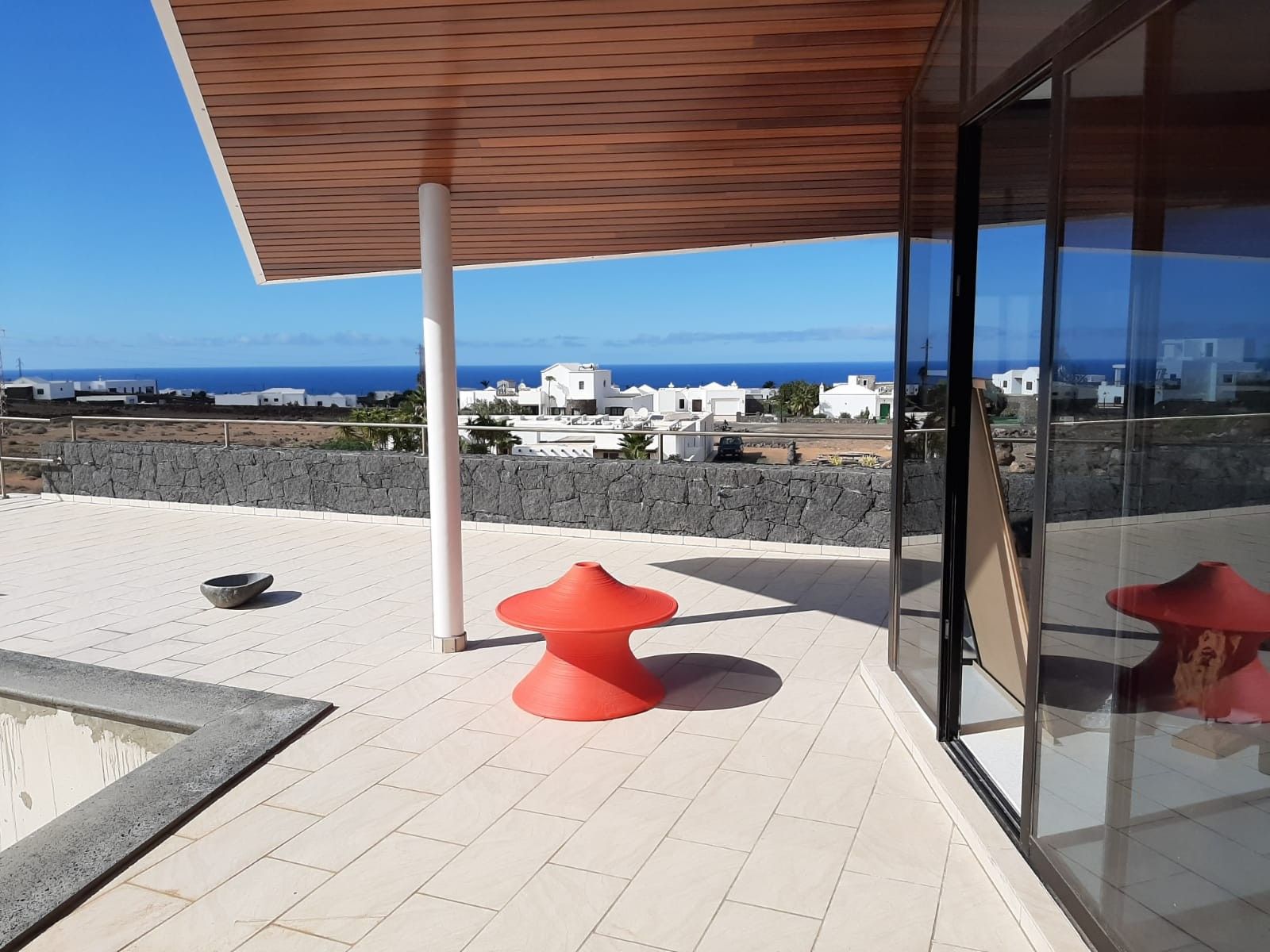 Eine Dachterrasse mit einer Steinsäule, einer Holzbalkendecke und Blick auf das Meer und die Stadt.