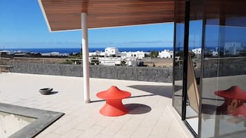 Eine Dachterrasse mit einer Steinsäule, einer Holzbalkendecke und Blick auf das Meer und die Stadt.
