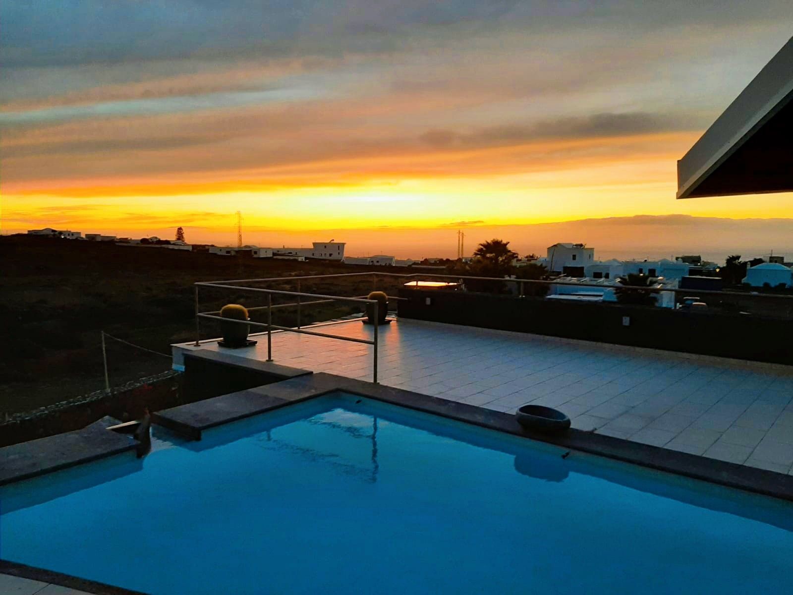 Une piscine sur le toit offrant une vue sur le coucher de soleil et les bâtiments environnants.
