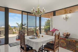 Un comedor con una mesa preparada para dos, una araña y vistas al mar.