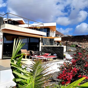 A modern two-story house with a balcony, outdoor seating, and a stone wall. - Apartment 'Atlantis' with Sea View, Pool and Air Conditioning (Las Breñas)