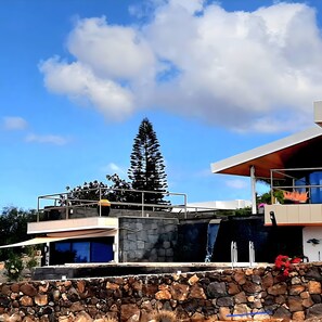 A modern house with a stone facade, a large tree, and a clear blue sky.