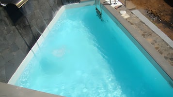 Ein Swimmingpool mit glatter, blauer Wasserfläche, einer Metallleiter und einer Steinmauer.