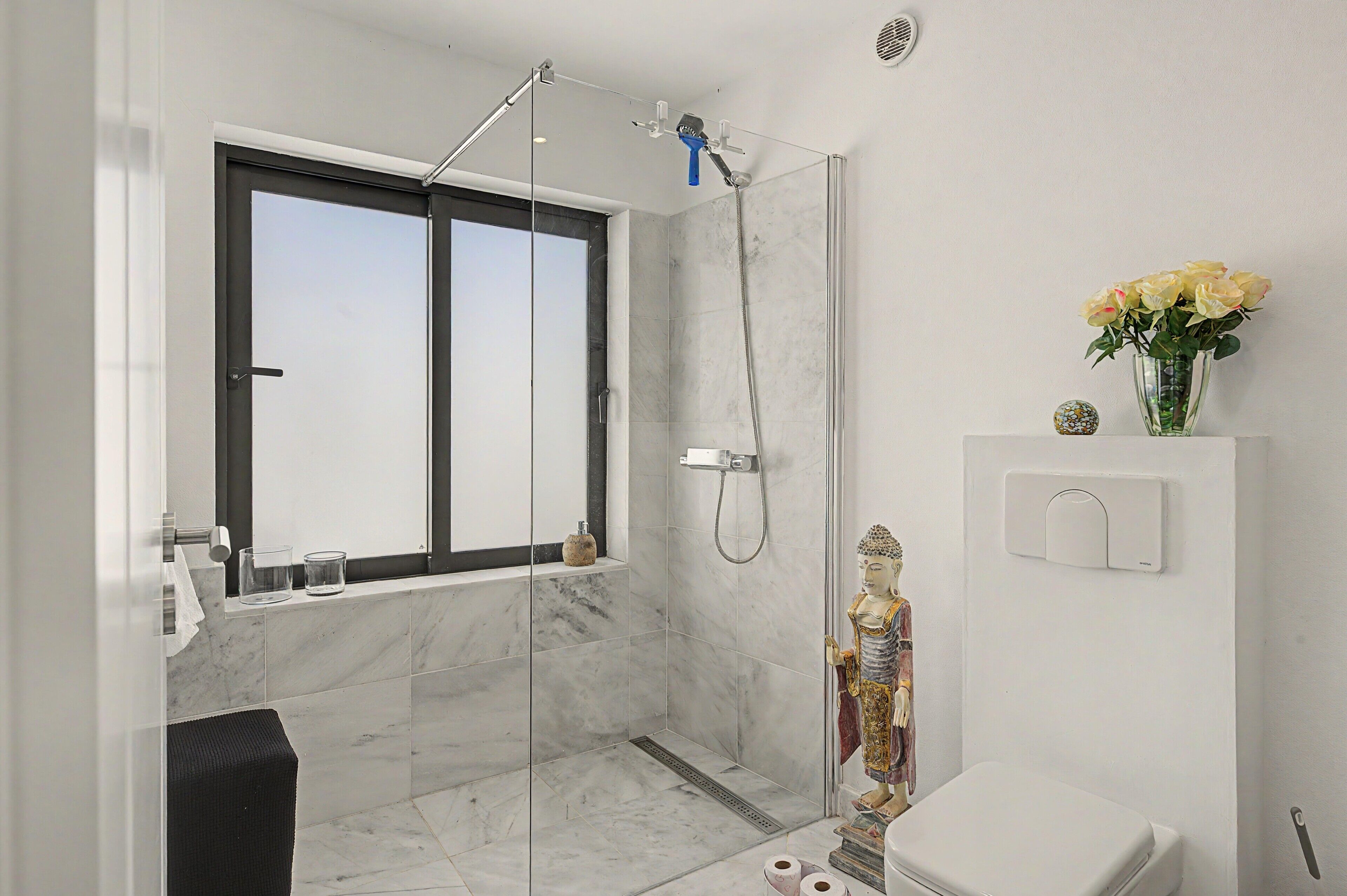 Un baño moderno con cabina de ducha de vidrio, inodoro, lavabo y ventana.