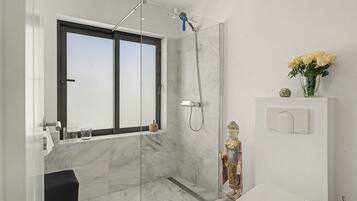 Un baño moderno con cabina de ducha de vidrio, inodoro, lavabo y ventana.