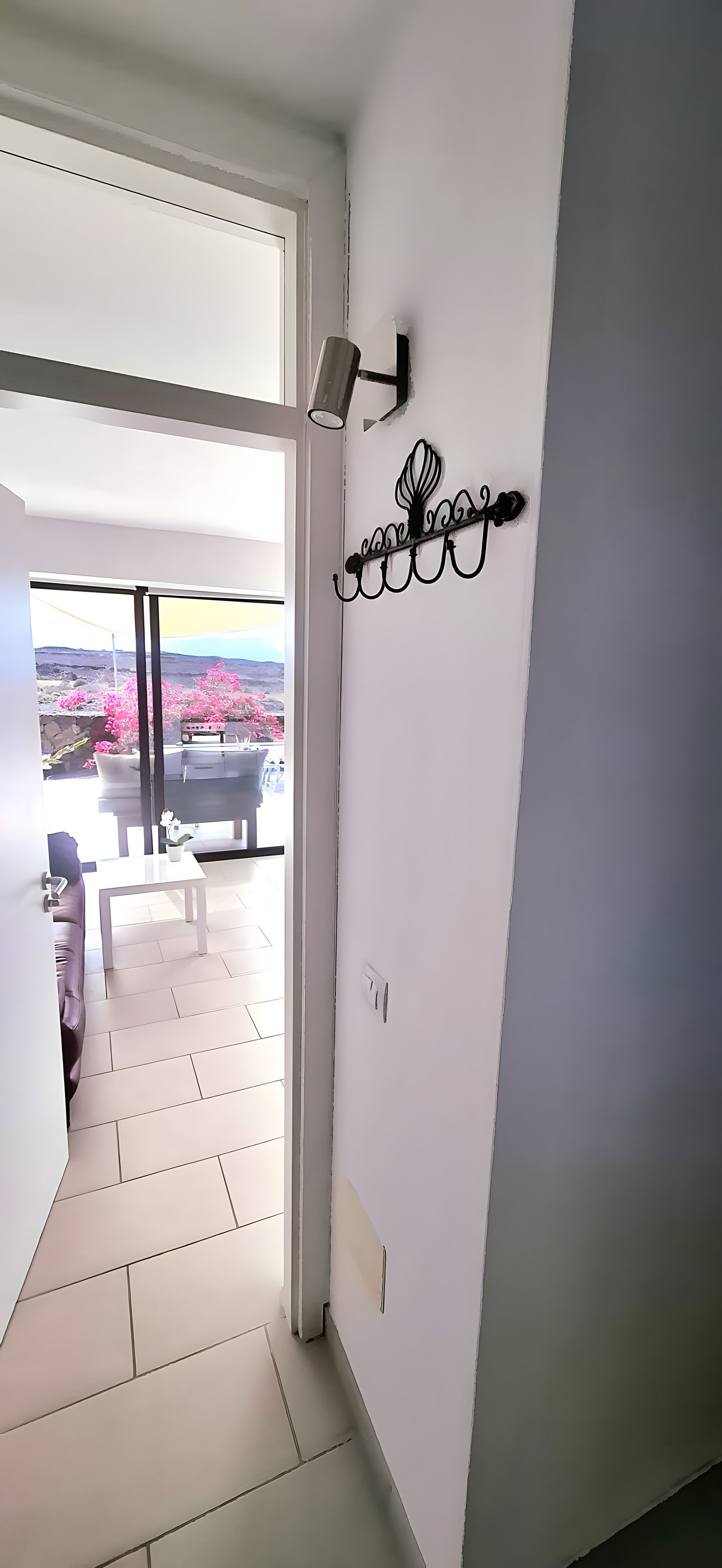 A hallway leading to a patio with a view of pink flowers and a table.