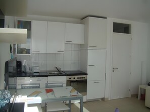 Une cuisine moderne avec des meubles blancs, un plan de travail noir, un évier, une cuisinière et une table à manger avec des chaises.