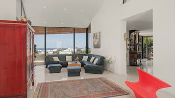 Ein modernes Wohnzimmer mit einer Eckcouch, einem roten Schrank und Blick auf das Meer.