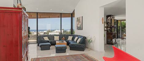 A modern living room with a sectional sofa, a red cabinet, and a view of the sea.