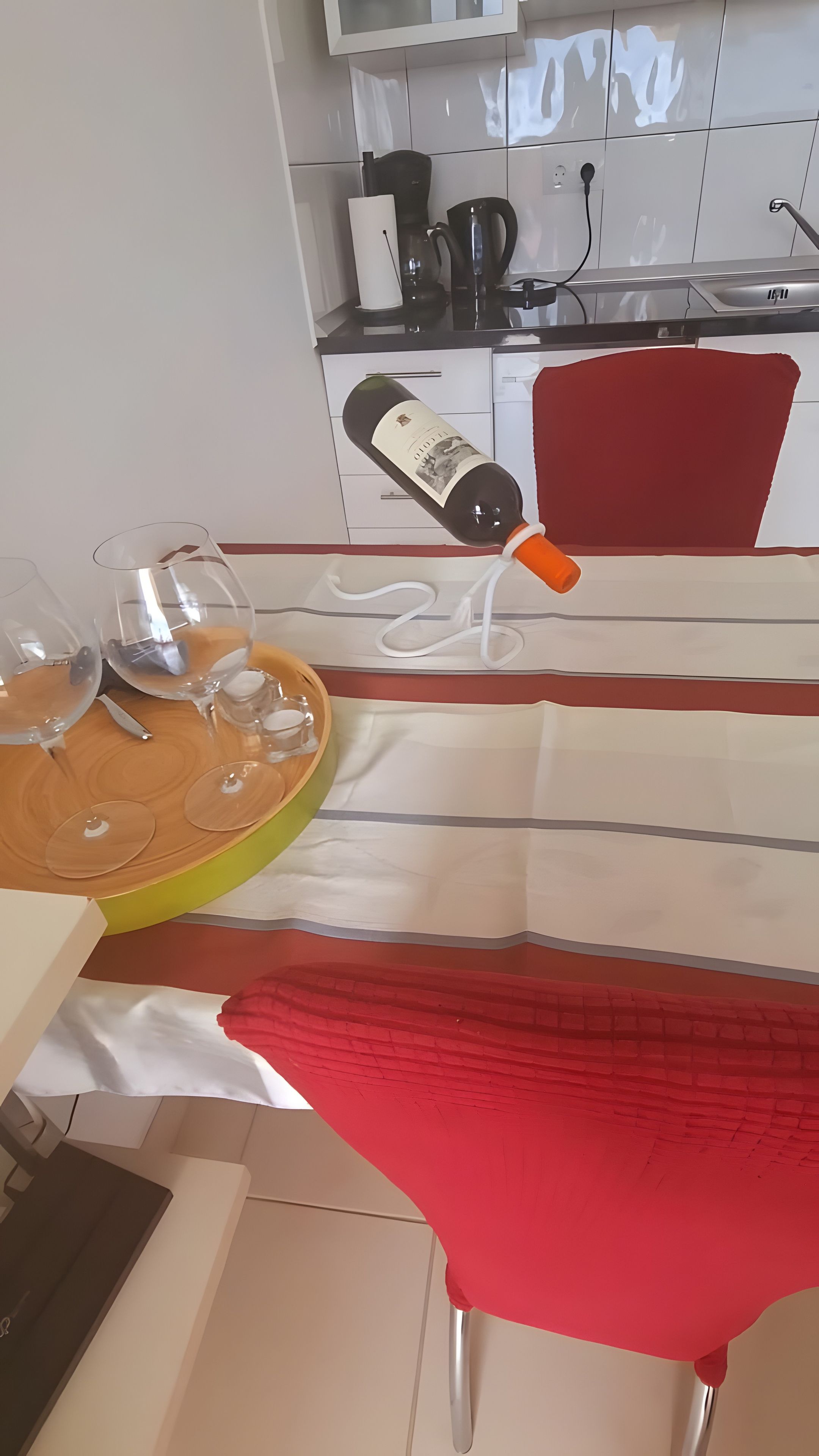 A dining area with a table set for two, a wine bottle, and a red umbrella.