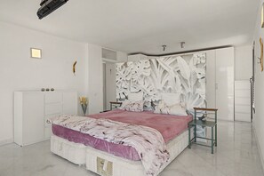 Une chambre à coucher comprenant un lit, une table de chevet, une commode et un mur orné d’un motif en forme de feuille.