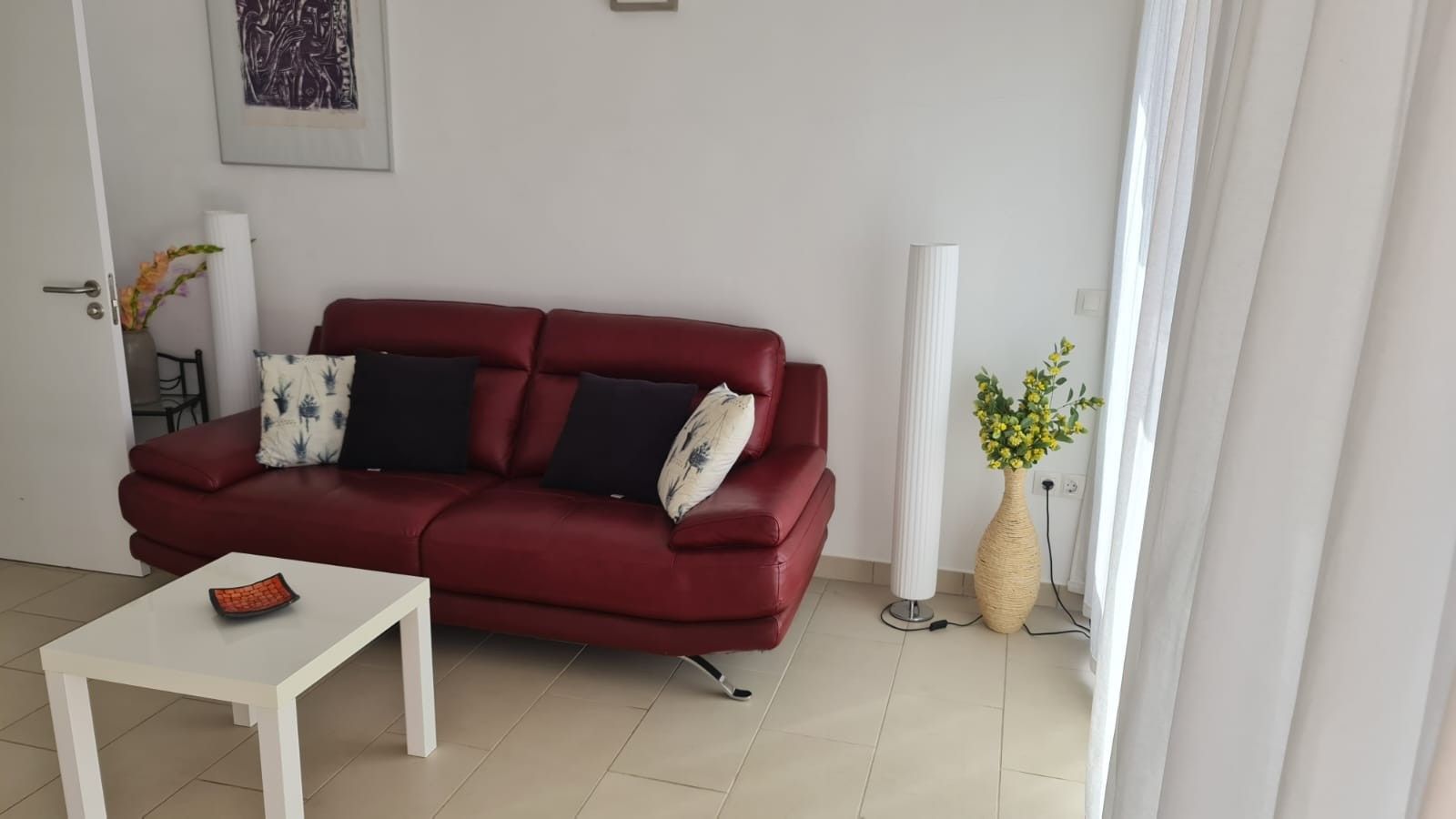 Ein rotes Sofa mit zwei schwarzen Kissen, ein weißer Couchtisch und eine Vase mit gelben Blumen.