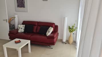 Ein rotes Sofa mit zwei schwarzen Kissen, ein weißer Couchtisch und eine Vase mit gelben Blumen.