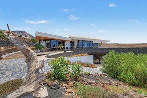 A modern house with a flat roof, large windows, and a stone wall. - Holiday Villa 'Atlantis' with Sea Views, Wi-Fi, and Air Conditioning (Las Breñas)