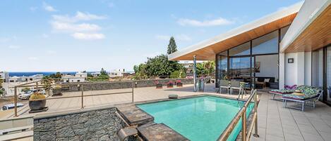 A rooftop pool area with a view of the sea, a covered seating area, and a stone wall.