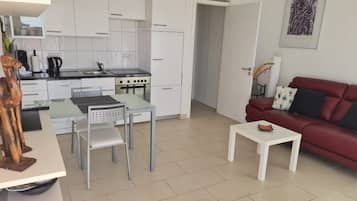 A modern kitchen with white cabinets, a dining table, and a red sofa in the living area.