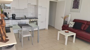 A modern kitchen with white cabinets, a dining table, and a red sofa in the living area. - Apartment Atlantis with Sea View, Wi-Fi and Air Conditioning (Las Breñas)
