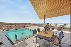 A poolside area with a table set for two, overlooking a volcanic landscape. - Apartment Atlantis with Sea View, Wi-Fi and Air Conditioning (Las Breñas)