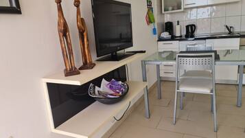 Une cuisine moderne équipée d’un téléviseur à écran plat, d’une table à manger avec une chaise, et d’une petite étagère sur laquelle se trouvent un bol et des magazines.