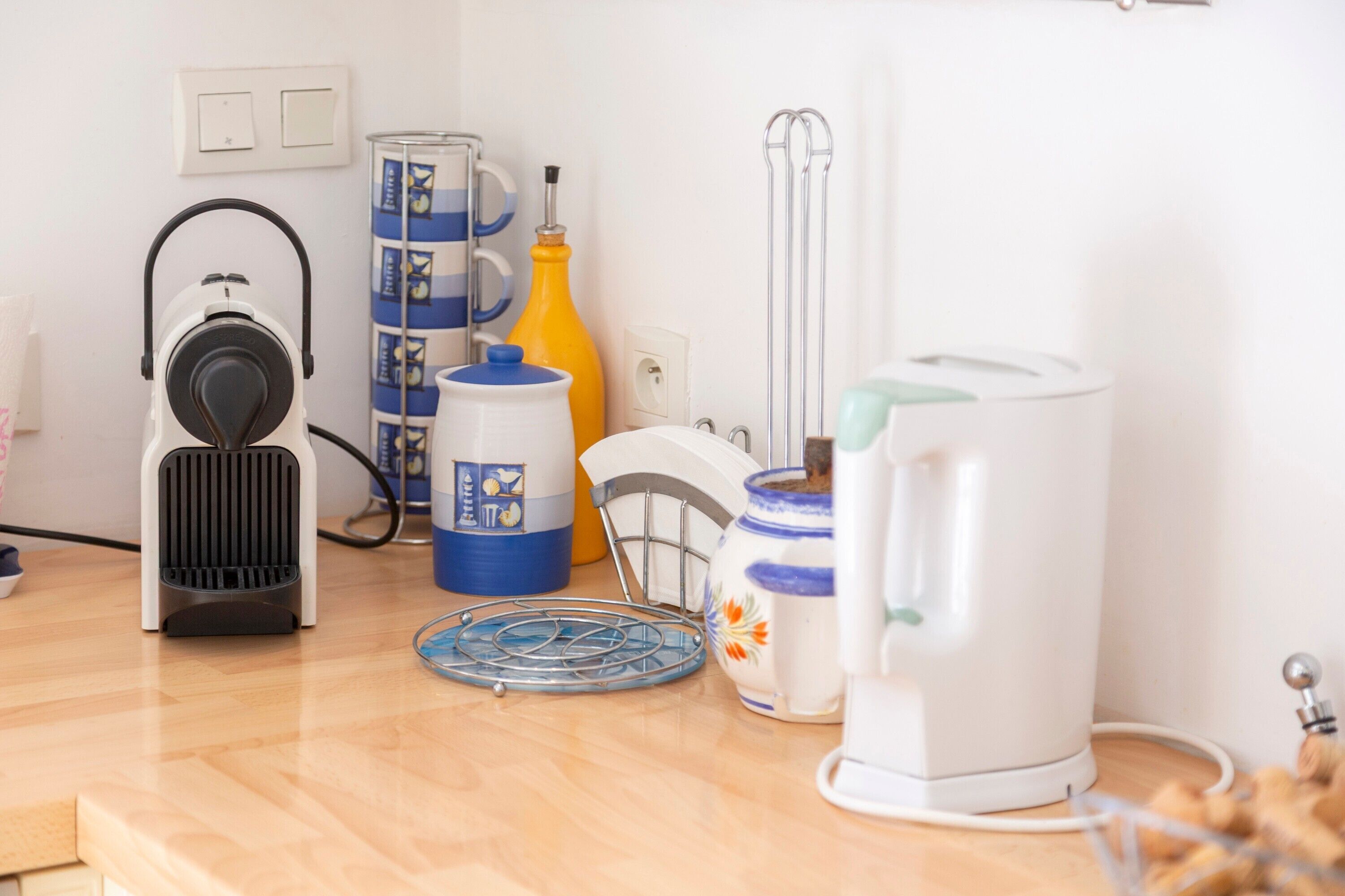 A kitchen with a coffee maker, a kettle, a bottle, and a dish rack.