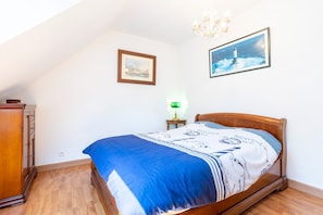 Ein Schlafzimmer mit einem hölzernen Bett, einem Nachttisch mit Lampe, einem gerahmten Bild eines Leuchtturms und einem Holzschrank.