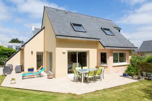 Een huis met een schuin dak, een terras met tuinmeubilair, en een grote schuifpui.