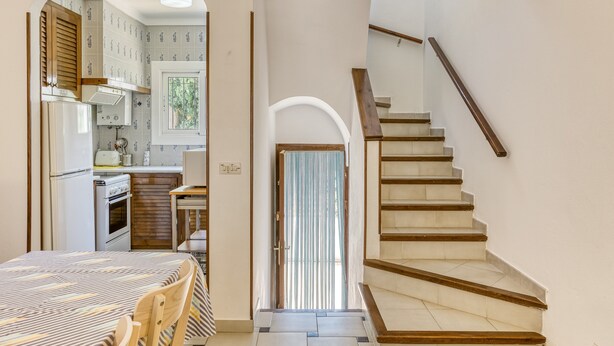 A staircase leading to a second floor, a kitchen with a refrigerator and stove, and a dining area with a table and chairs. - Holiday Home 'Palau 100m Playa' with Private Terrace and Wi-Fi (L'Escala)
