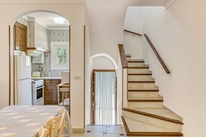 Una escalera que lleva a un segundo piso, una cocina con refrigerador y estufa, y un comedor con mesa y sillas.