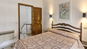 A bedroom with a bed, a wooden door, a radiator, and a wall-mounted light fixture. - Holiday Home 'Palau 100m Playa' with Private Terrace and Wi-Fi (L'Escala)
