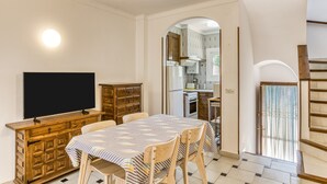 A dining area with a TV, wooden cabinet, and a patterned tablecloth. - Holiday Home 'Palau 100m Playa' with Private Terrace and Wi-Fi (L'Escala)