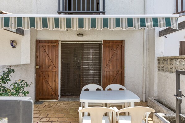 Une terrasse avec une table et des chaises, une porte en bois et un auvent à rayures.