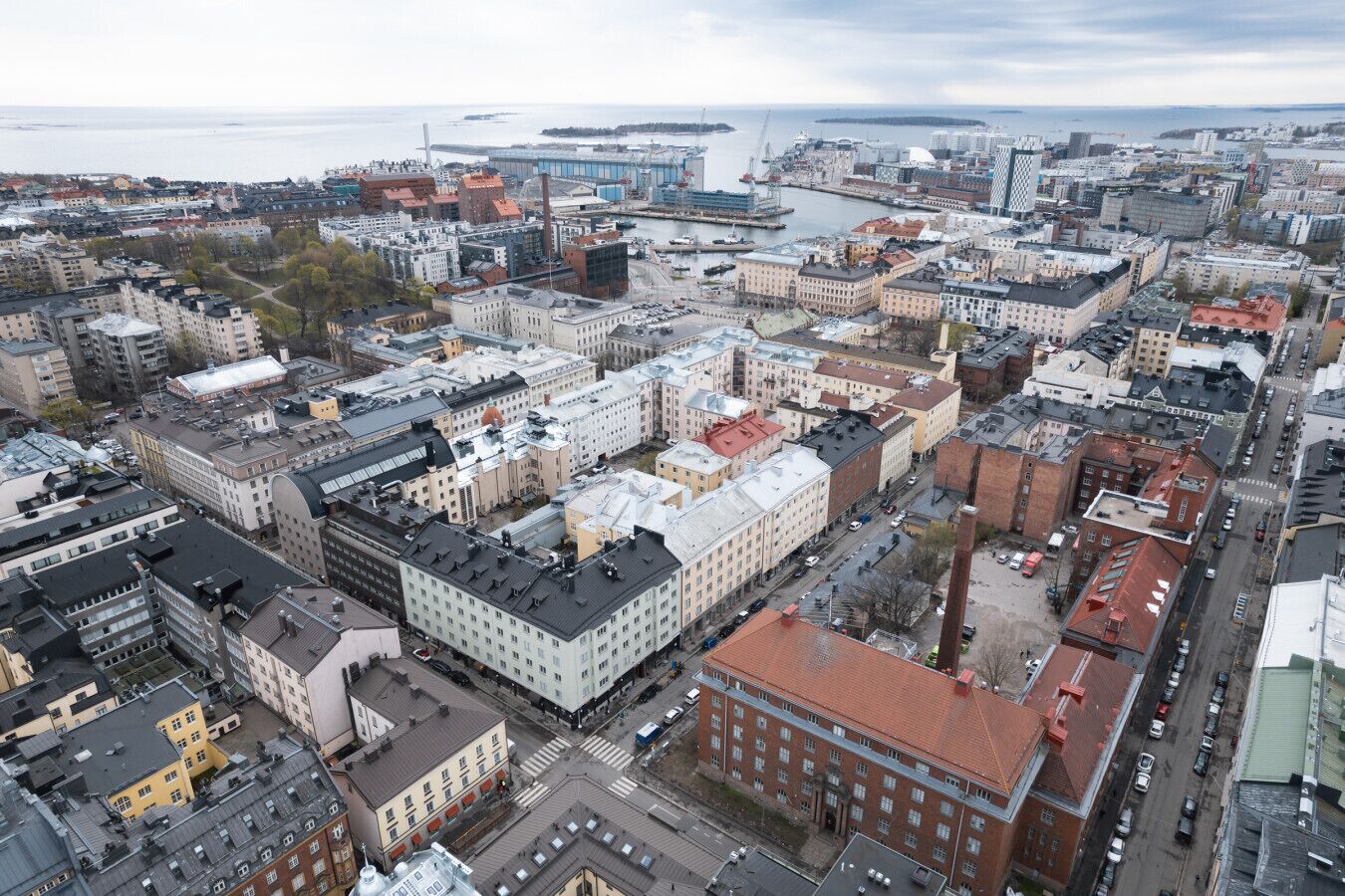 An aerial view of a cityscape with a mix of modern and traditional buildings, a prominent waterfront, and a busy street with vehicles.