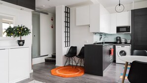 Una cucina moderna con mobili bianchi, un forno a microonde, una lavatrice e un'area pranzo con due sedie nere.
