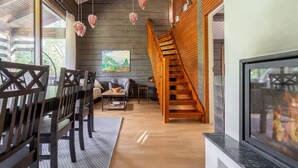 A modern interior with a wooden staircase, a dining area with dark chairs, and a living room with a sofa and a painting.
