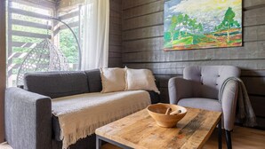 A cozy room with a grey sofa, a grey armchair, a wooden table with a bowl, and a painting of a landscape on the wall.