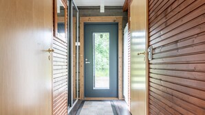 A hallway with wooden paneling, a dark grey door, and a black mat at the entrance.