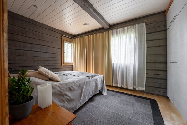 A bedroom with a bed, a nightstand, a potted plant, and a window with curtains.